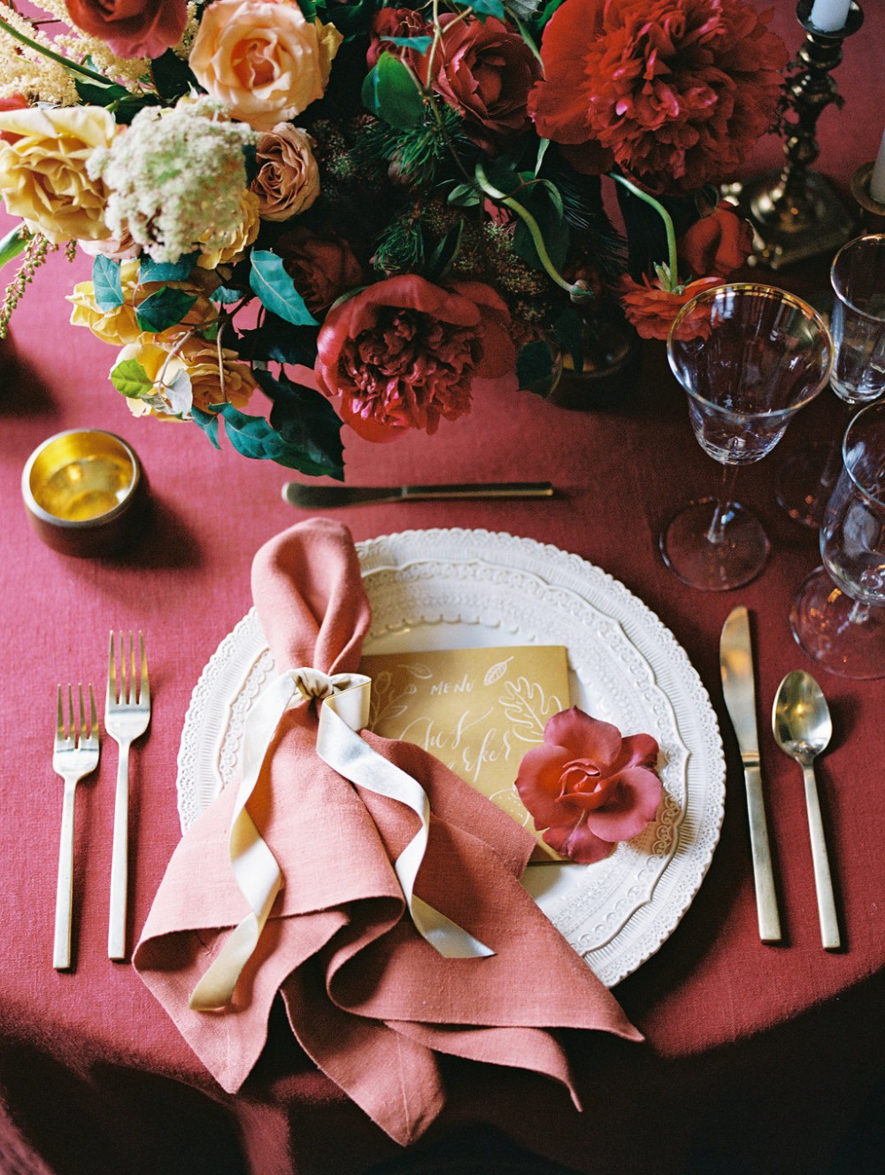 A warm red and orange place setting with a cream charger plate and a mustard yellow meu